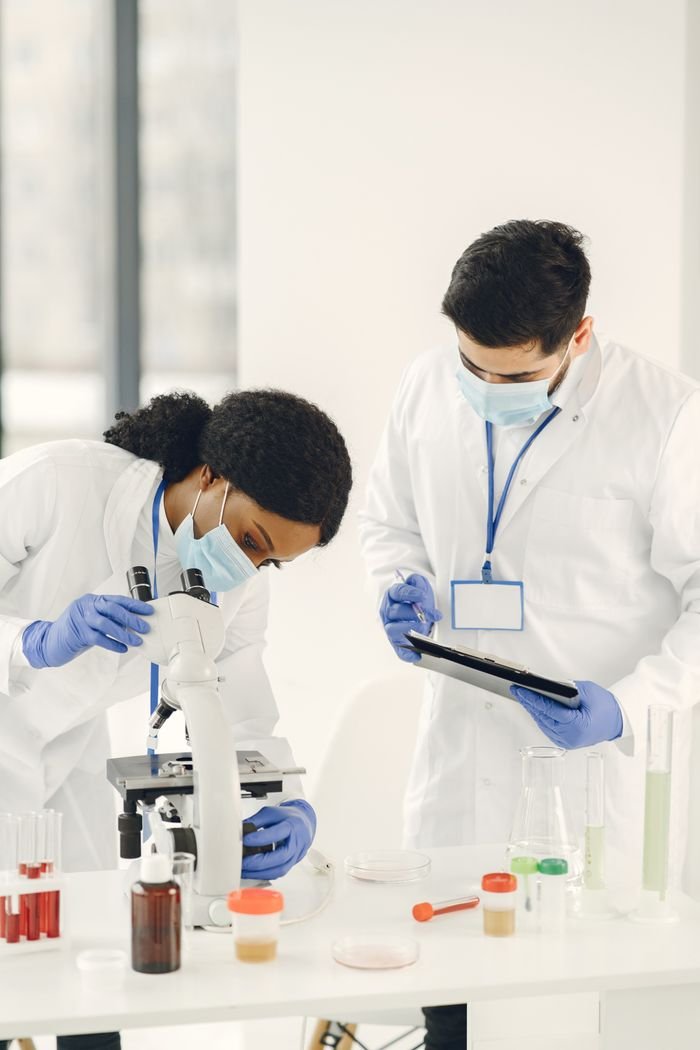 Two scientists in lab coats examining samples using a microscope, highlighting teamwork in research.